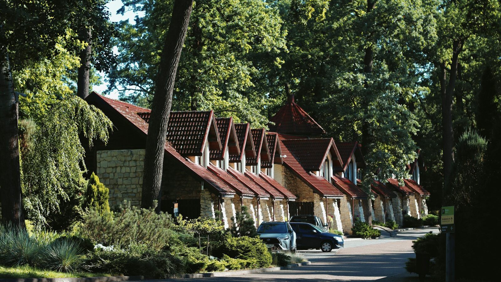 Bungalows met puntdaken tussen de bomen van een vakantiepark